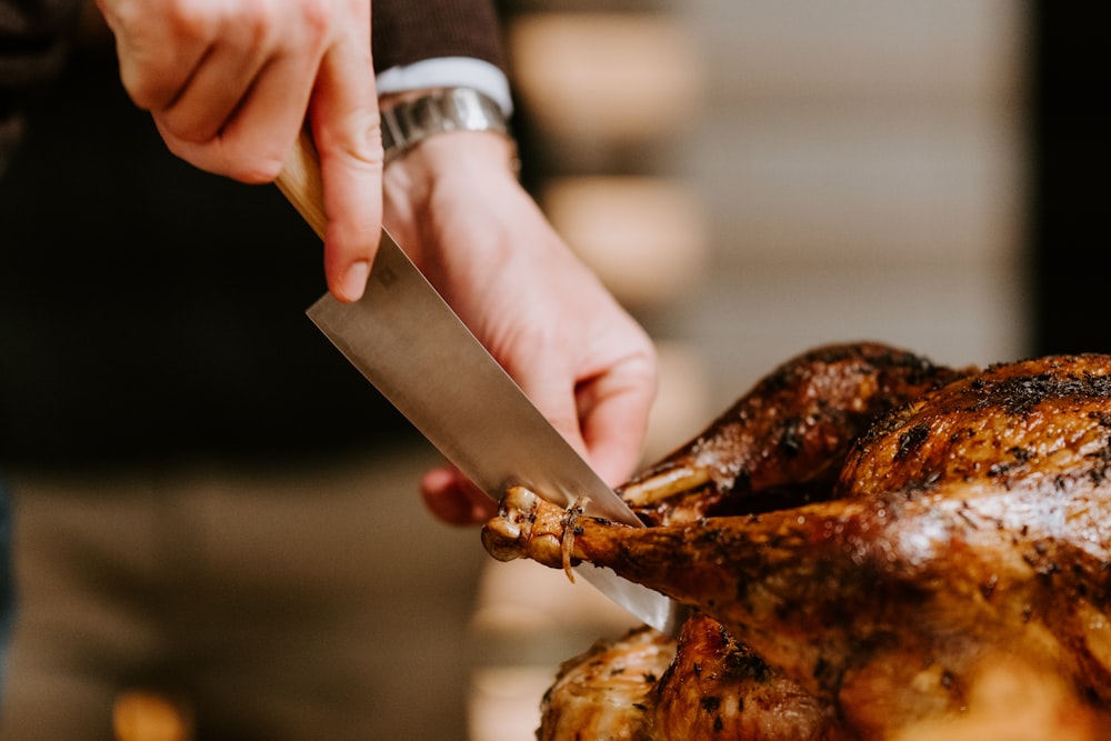 person holding knife and grilled chicken