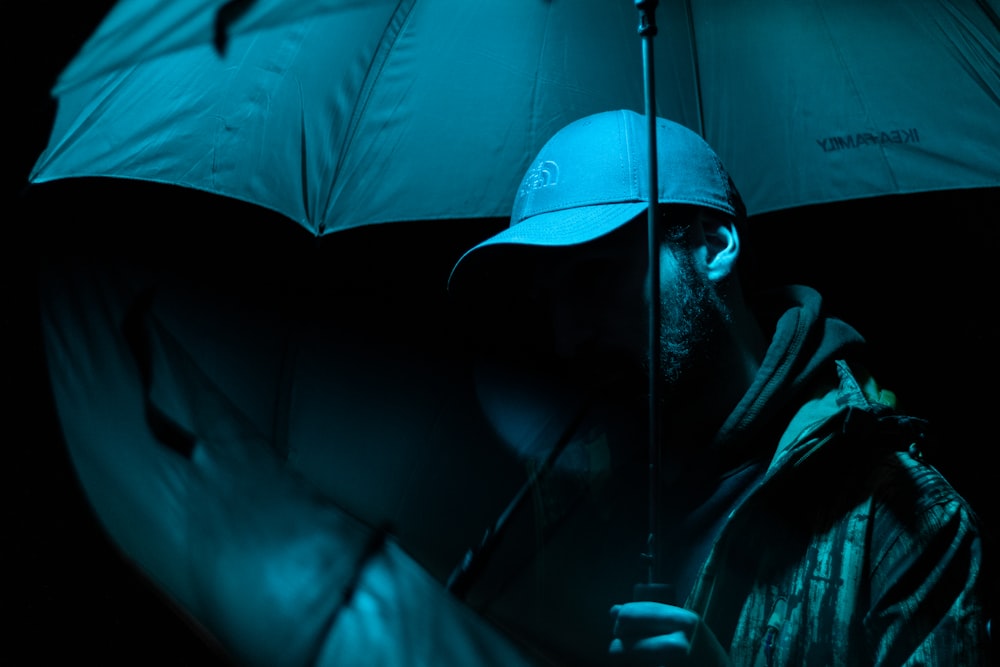man in black hoodie and blue fitted cap holding umbrella