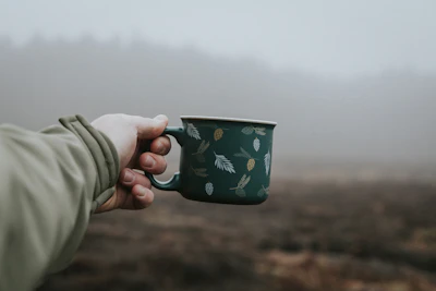 A hand holding a tumbler outdoors with a blurred background of morning nature.