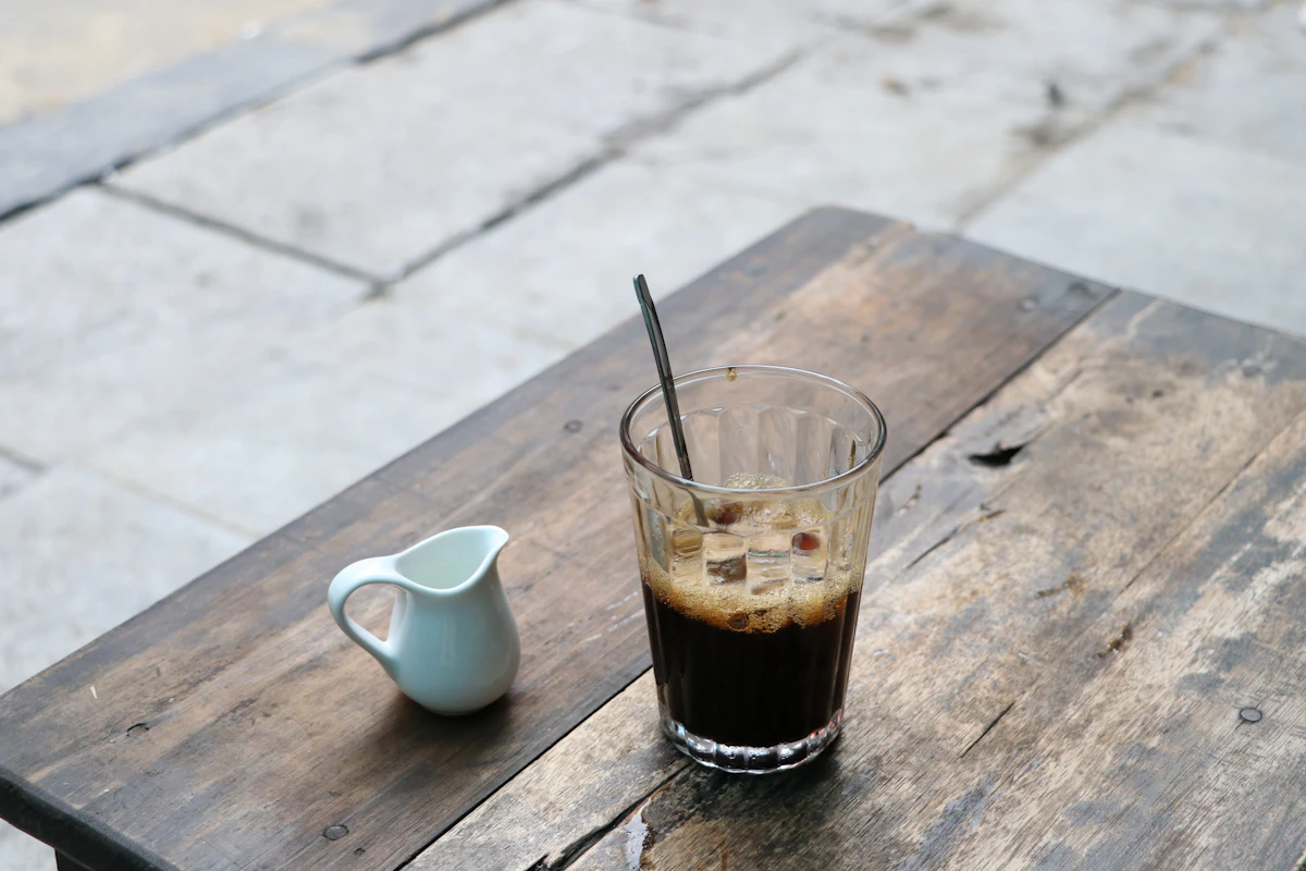 Ly cold brew cà phê đen cùng bình sữa nhỏ trên bàn gỗ