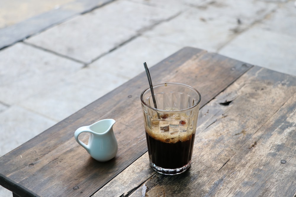 clear glass mug with black liquid on brown wooden table