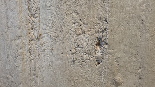 A close-up view of a rough, textured concrete wall with evident wear and damage. There are visible cracks and small holes scattered across the surface.