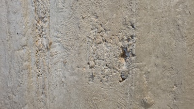 A close-up view of a rough, textured concrete wall with evident wear and damage. There are visible cracks and small holes scattered across the surface.