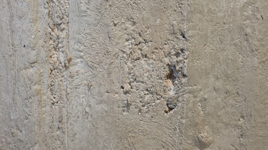 A close-up view of a rough, textured concrete wall with evident wear and damage. There are visible cracks and small holes scattered across the surface.
