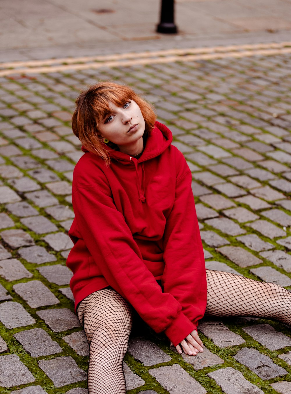 woman in red hoodie sitting on gray brick floor during daytime