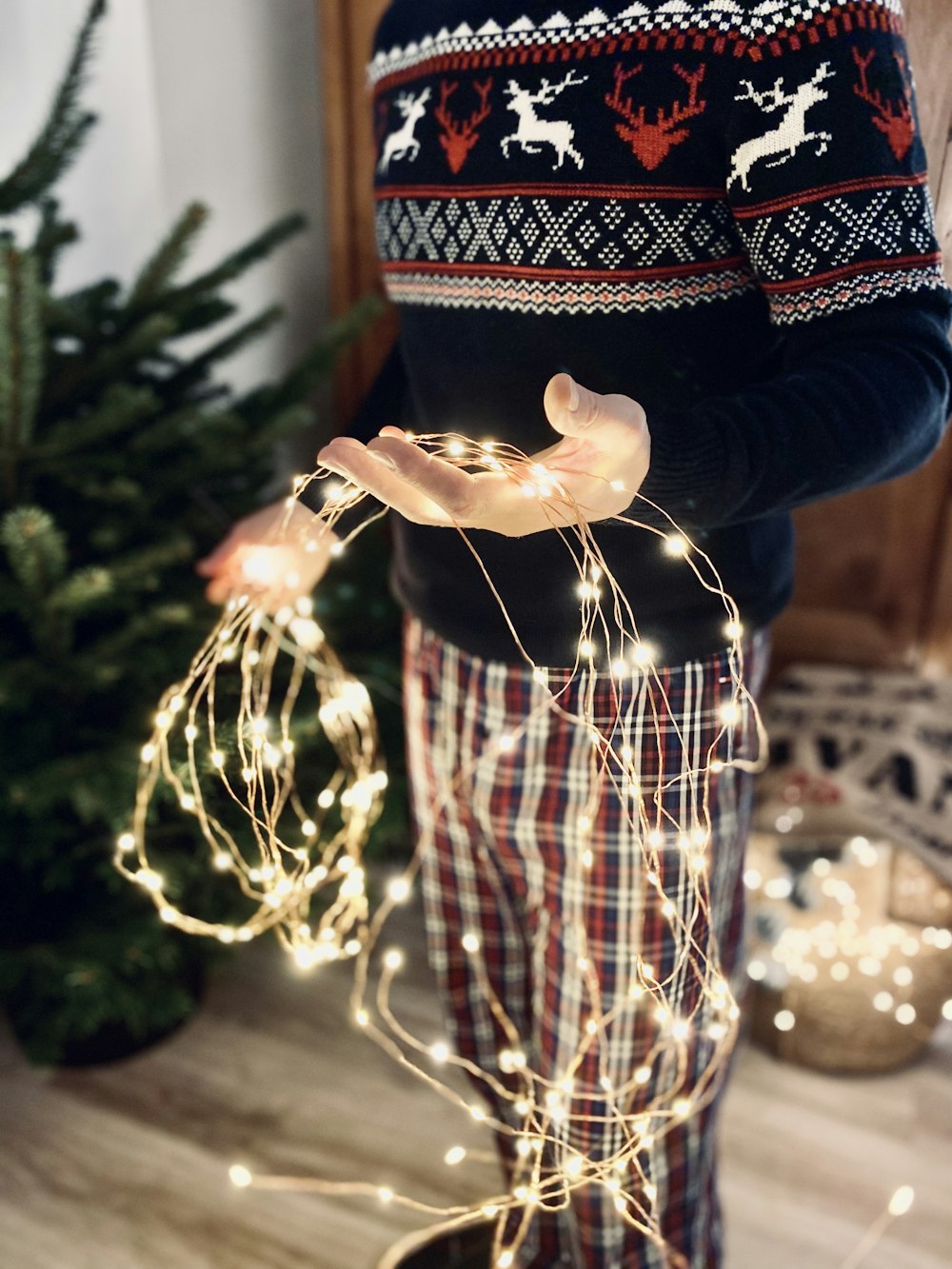 person in blue sweater holding gold and red christmas tree ornament