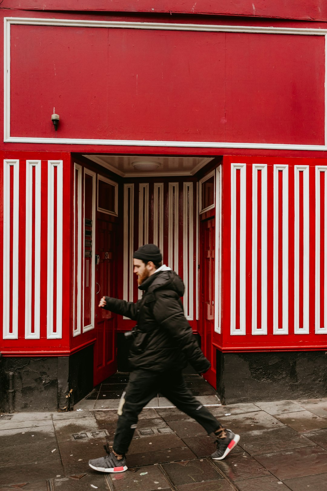 man in black jacket and black pants standing beside red wooden door