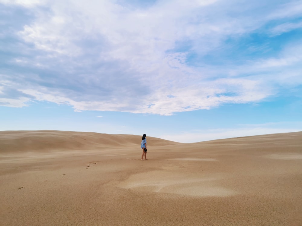 Person in schwarzer Jacke, die tagsüber auf braunem Sand unter blauem Himmel spazieren geht