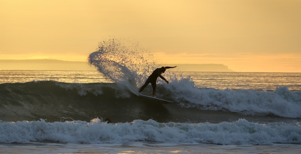 hombre surfeando en las olas del mar durante la puesta del sol