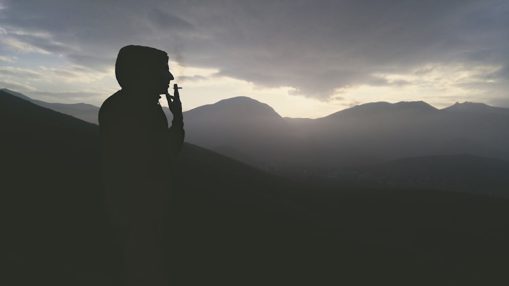 silhouette of man standing on top of mountain during sunset