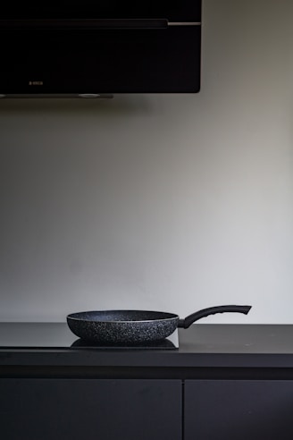 A sleek, modern non-stick frying pan resting on a wooden kitchen countertop with fresh vegetables nearby.