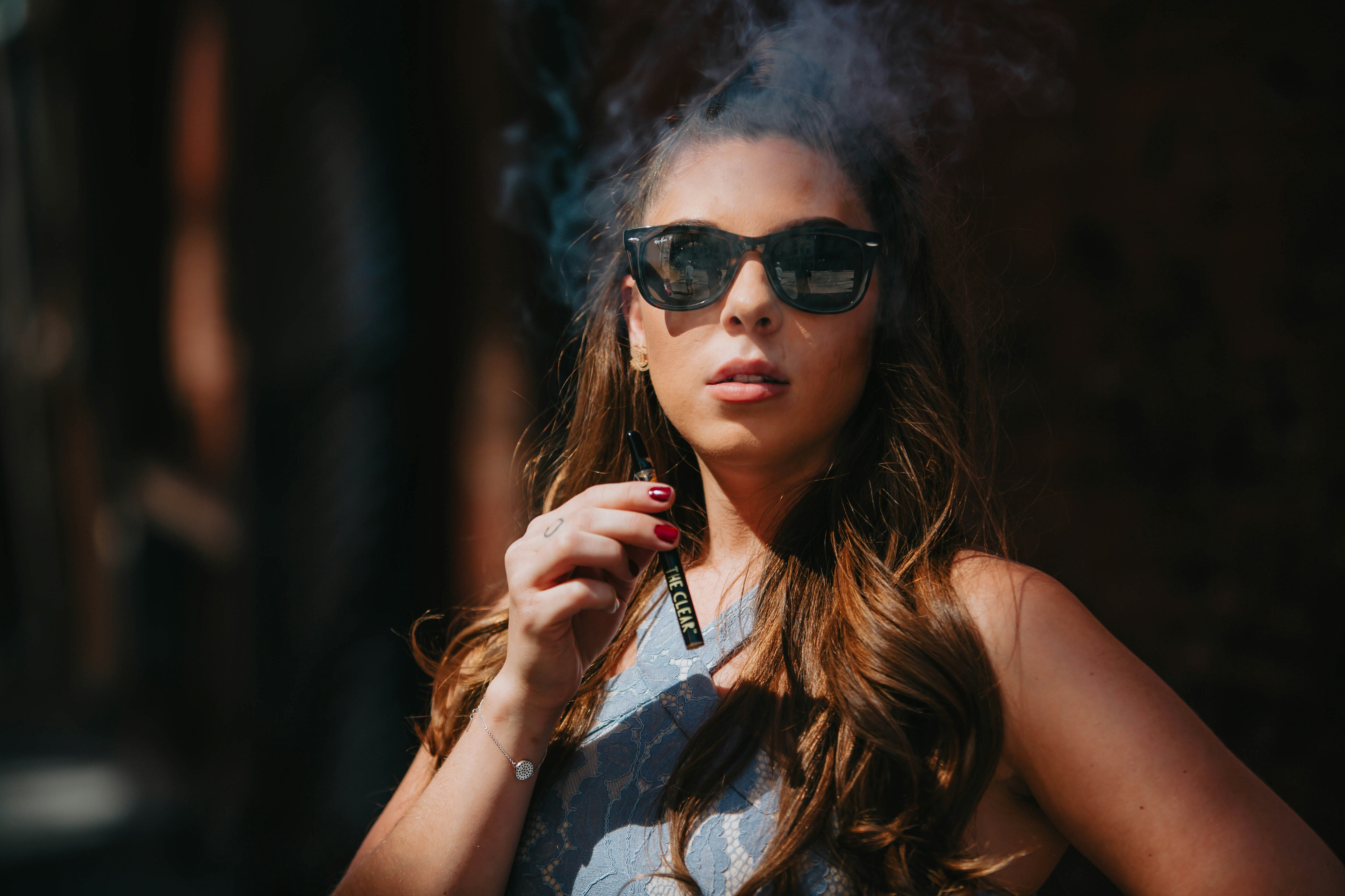 Woman, over 21, in a dress and sunglasses is consuming cannabis distillate from The Clear THC cartridge. The Clear produces premium cannabis products. Find out more at https://theclearbrands.com/