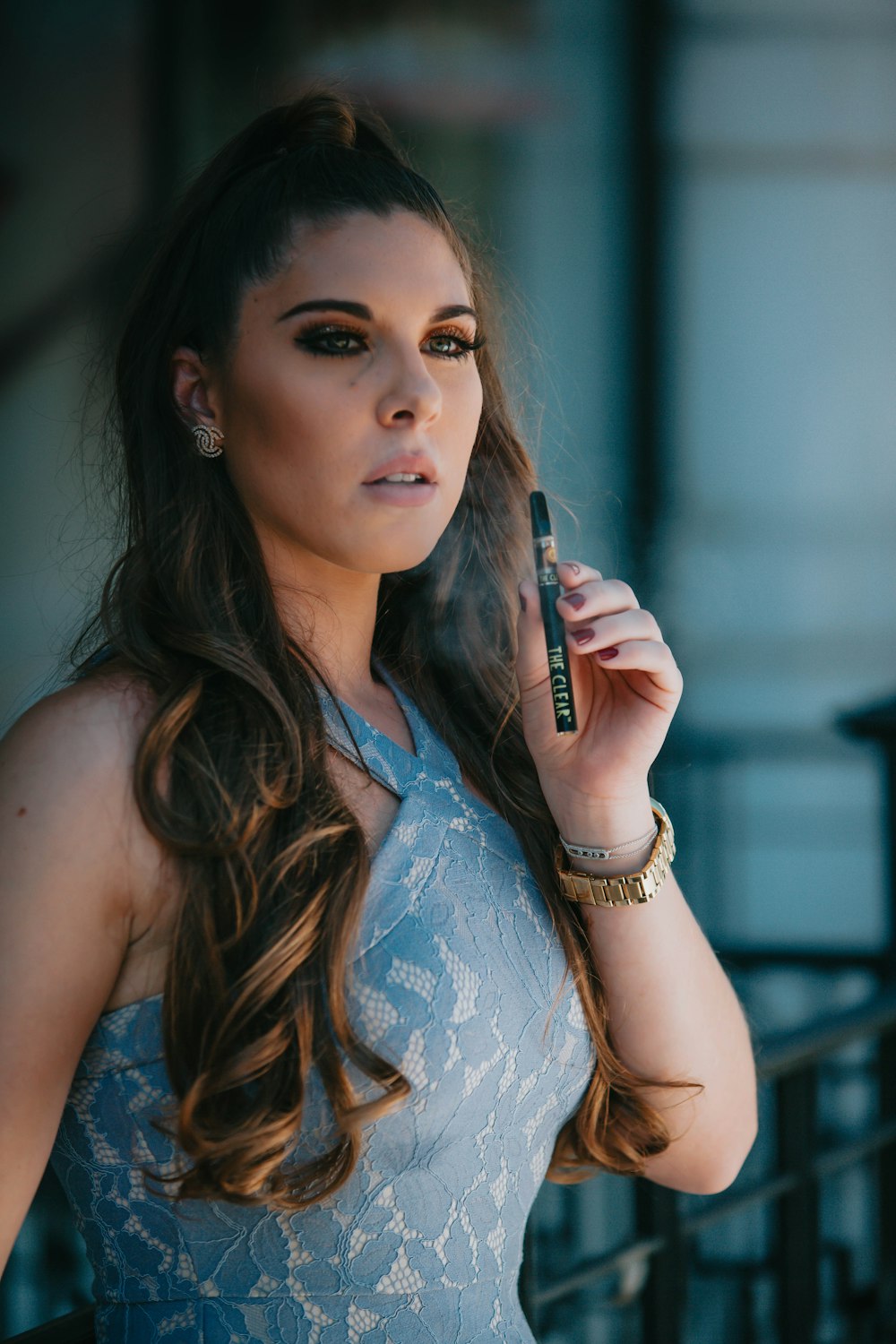 Femme en robe sans manches fleurie blanche et bleue tenant une vape de type tube noir et argent