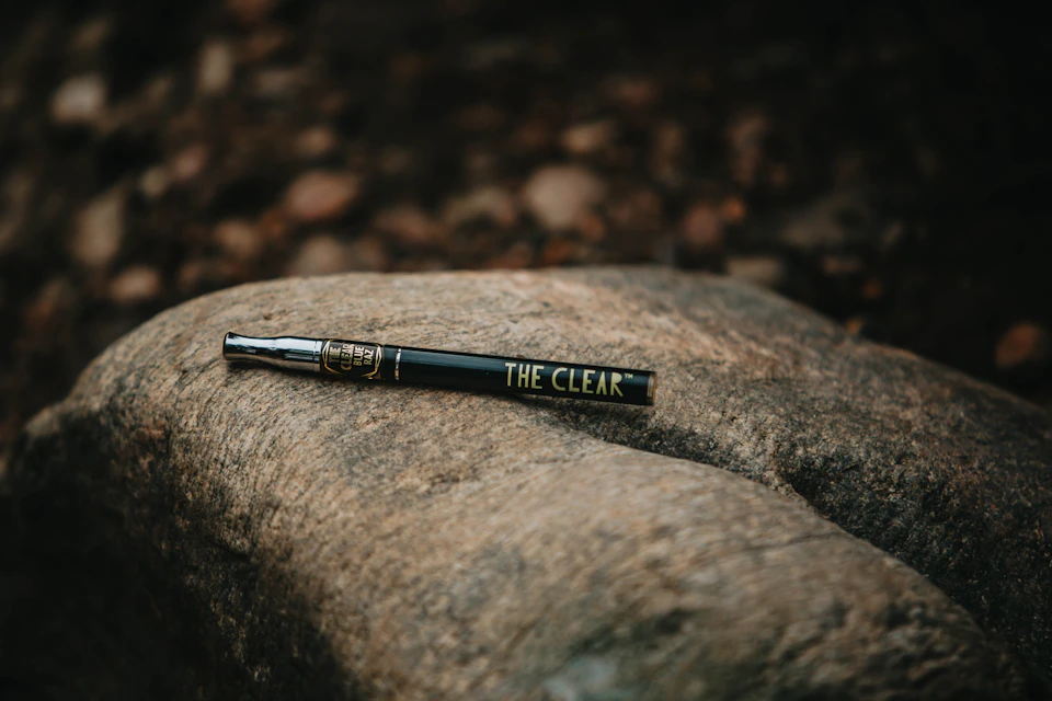 Black pen with gold lettering rests on a rough-textured rock, partially to the left