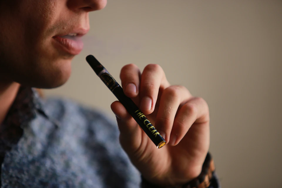 Close-up view of hand holding electronic cigarette with yellow label "THE CLEAN" visible