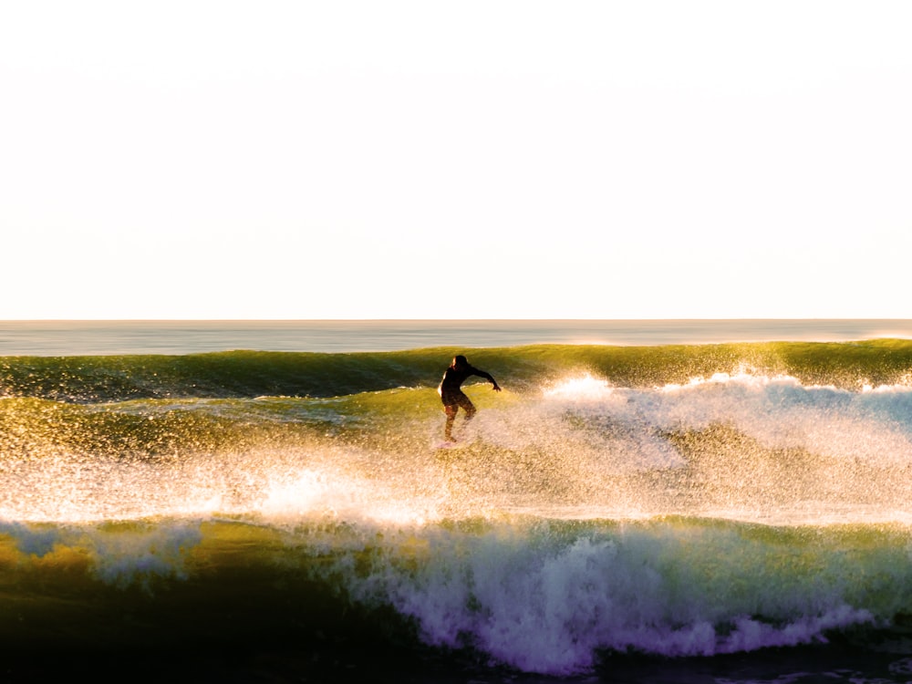 hombre con traje de neopreno negro surfeando en las olas del mar