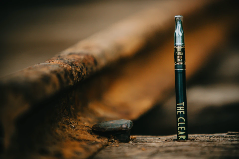 Black electronic cigarette resting on wooden surface with silver top and rusty metal railing