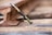 A vape pen labeled 'THE CLEAR' is resting diagonally against a rusty railroad track. The background features blurred wooden railroad ties and metal tracks, with a shallow depth of field focusing on the vape pen.