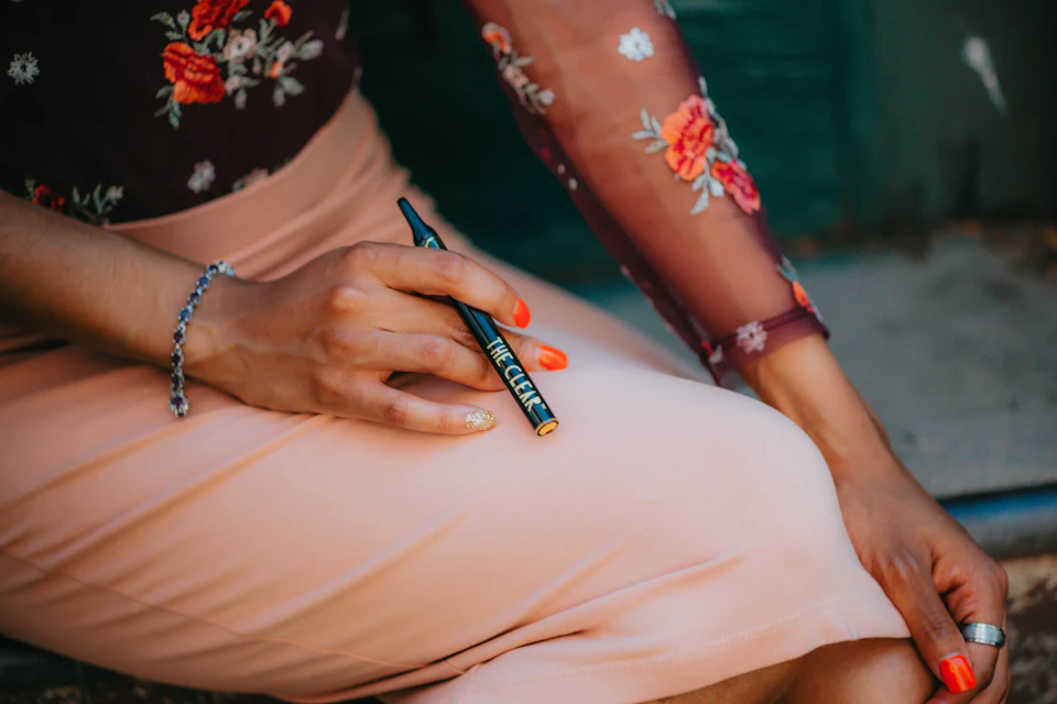 Person sits on concrete surface with legs crossed, wearing pink skirt and red nail polish