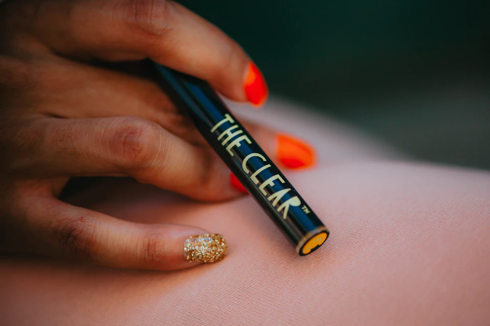 Hand holds black cigarette with gold glittery nail polish, positioned over pink surface