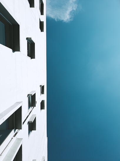 Painter applying fresh white paint on a modern building exterior under clear blue sky.