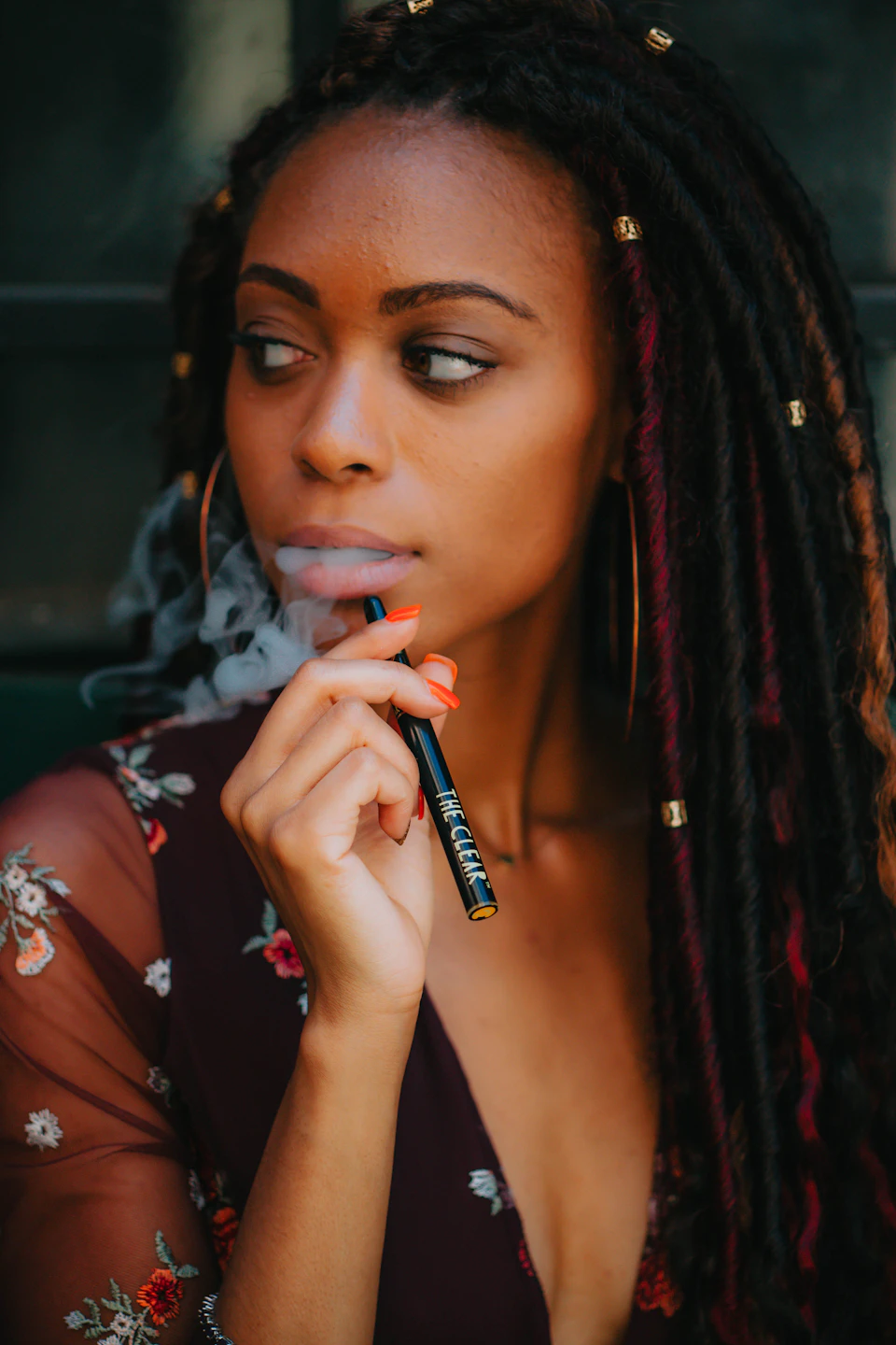 Young woman smokes a black cigarette while wearing a floral dress and long dark hair