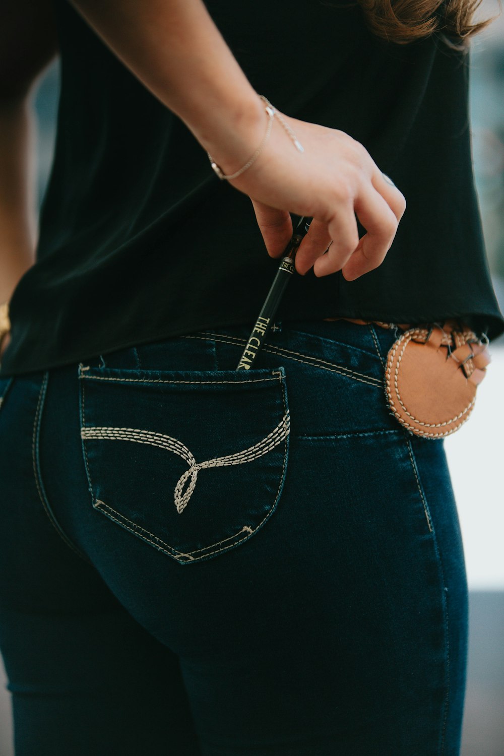 Personne en jean bleu tenant un sac à bandoulière en cuir noir