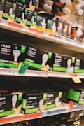 Shelves filled with various types of boxed LED light bulbs are visible, prominently featuring the NOMA brand. The boxes are black with green accents and display images of light bulbs and energy efficiency ratings. Price tags and product information are visible on the shelf edges.