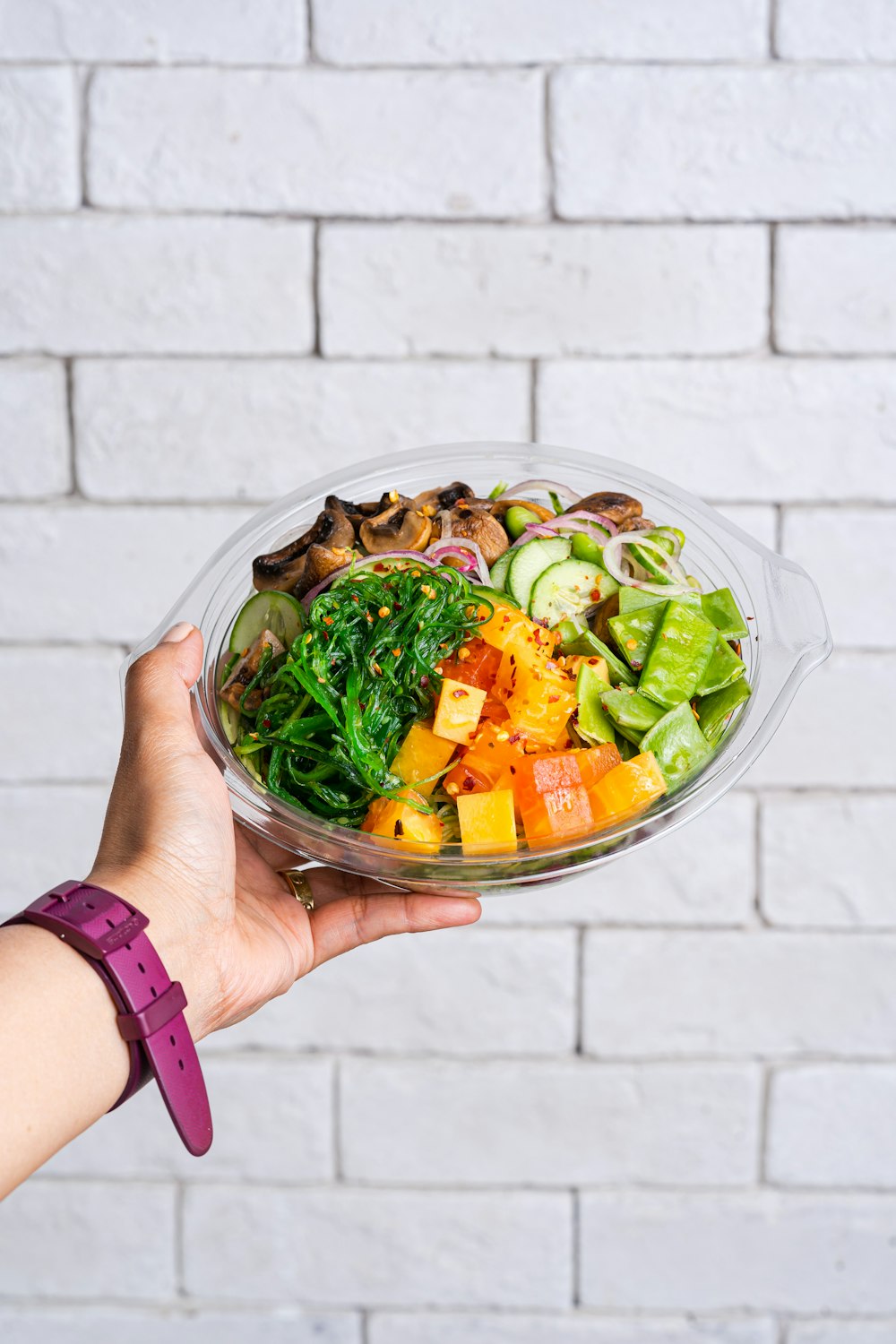 Persona sosteniendo ensalada de verduras en un recipiente de vidrio transparente