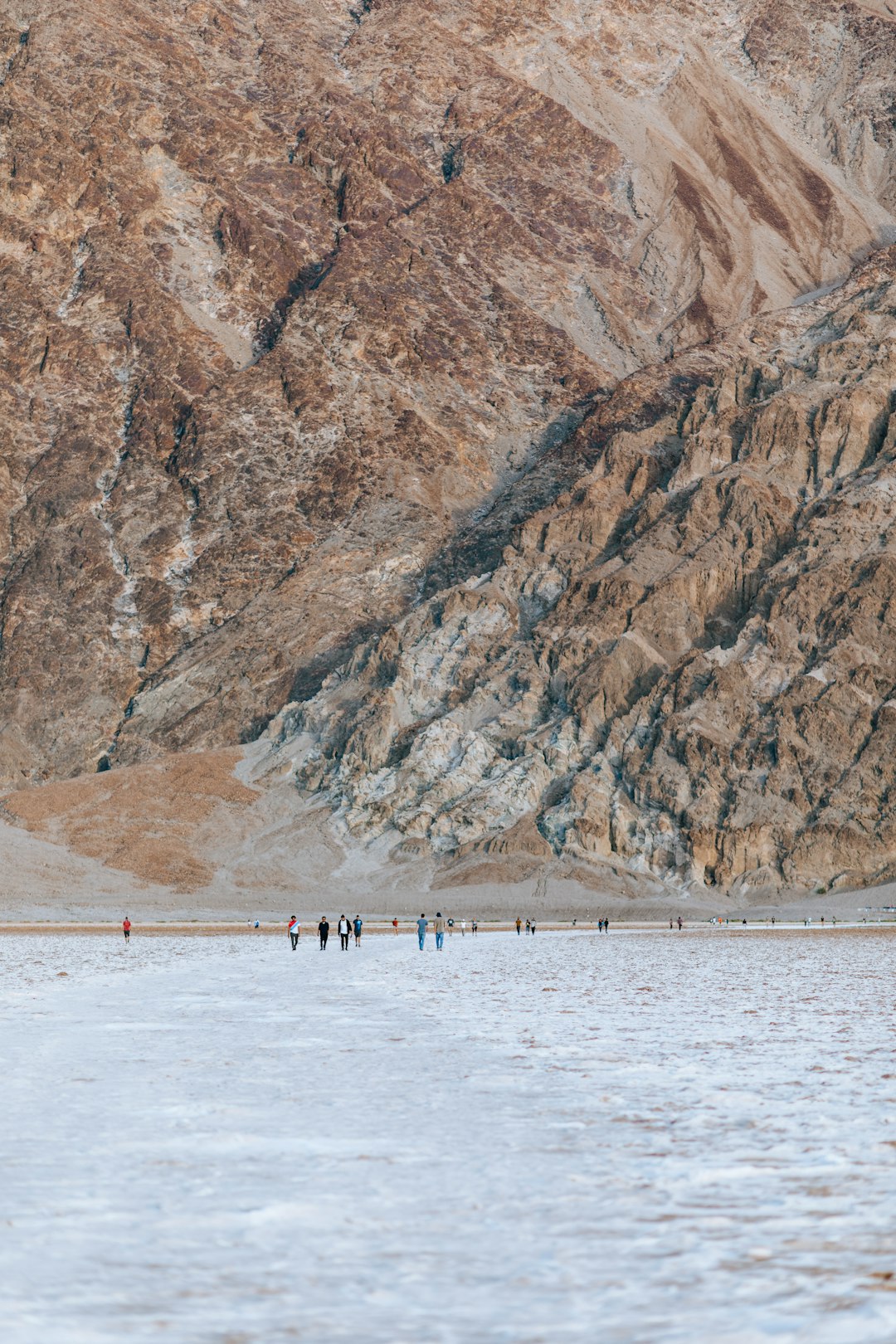 people on beach near brown rocky mountain during daytime