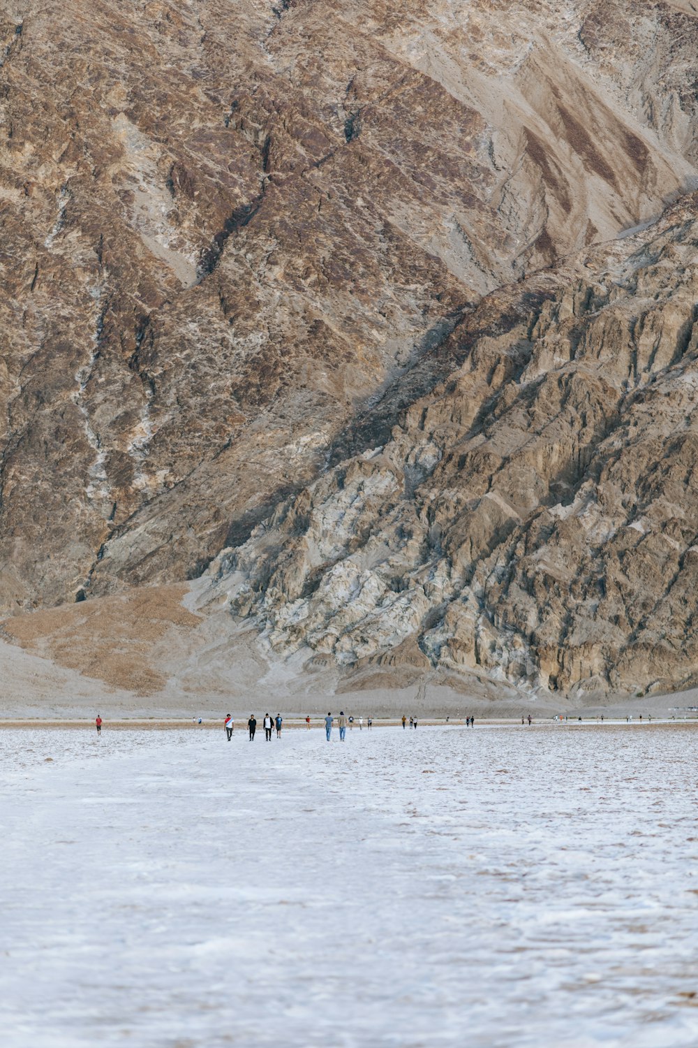 people on beach near brown rocky mountain during daytime