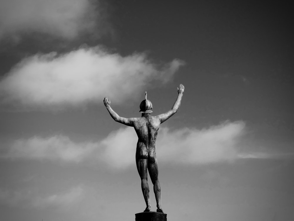 右手の彫像を掲げる男のグレースケール写真