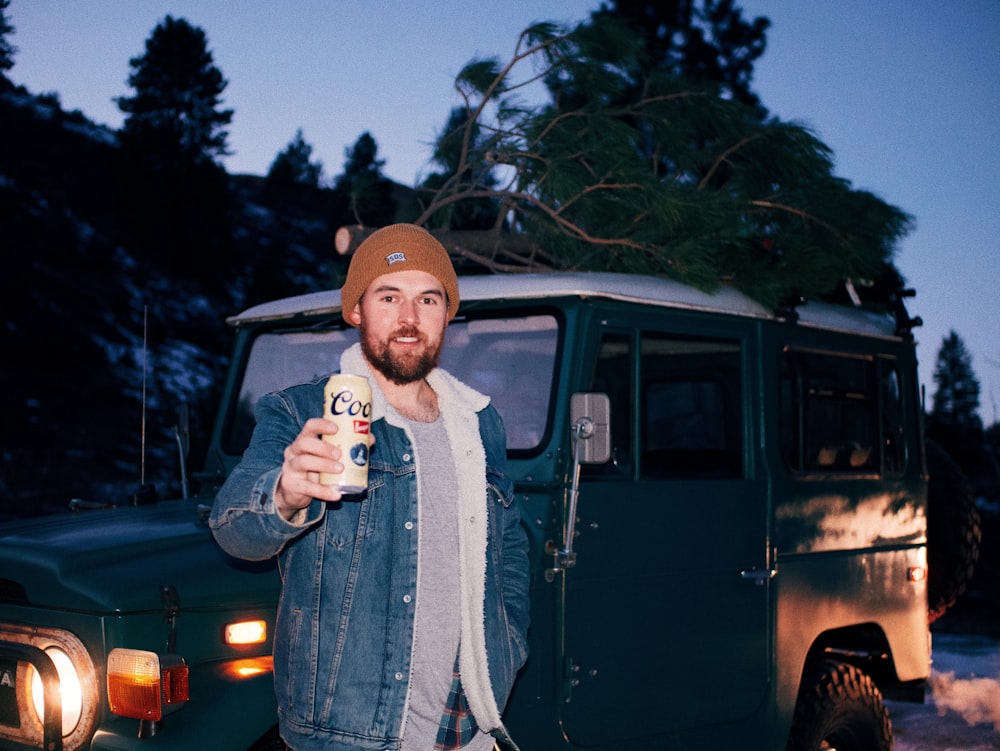 man in gray coat wearing brown knit cap standing beside black suv during daytime