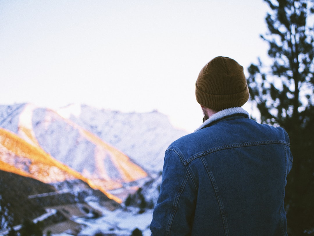 man in black jacket and brown knit cap standing on mountain during daytime