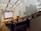 A modern lecture hall with tiered wooden seating, filled with students attentively watching a presentation on a large screen. The room is spacious with sleek architectural design, featuring high ceilings and white walls with geometric patterns. There is a lecturer standing near the podium delivering a lecture.