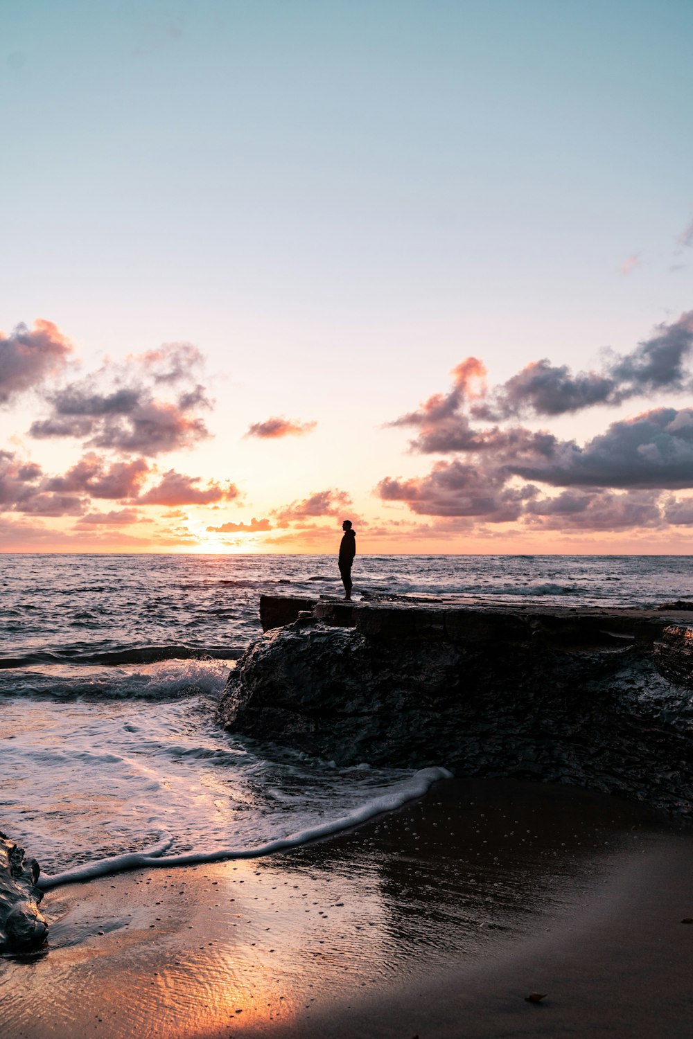person standing on rock near sea during sunset