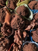 A variety of chocolate confections, including truffles dusted with cocoa powder and clusters of chocolate-covered nuts, are arranged together. The sweets are presented in colorful paper cups, adding a visually appealing contrast.