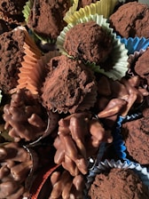 A variety of chocolate confections, including truffles dusted with cocoa powder and clusters of chocolate-covered nuts, are arranged together. The sweets are presented in colorful paper cups, adding a visually appealing contrast.