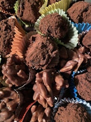 A variety of chocolate confections, including truffles dusted with cocoa powder and clusters of chocolate-covered nuts, are arranged together. The sweets are presented in colorful paper cups, adding a visually appealing contrast.