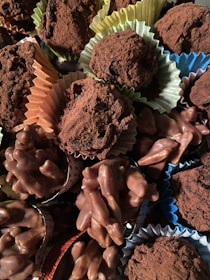 A variety of chocolate confections, including truffles dusted with cocoa powder and clusters of chocolate-covered nuts, are arranged together. The sweets are presented in colorful paper cups, adding a visually appealing contrast.