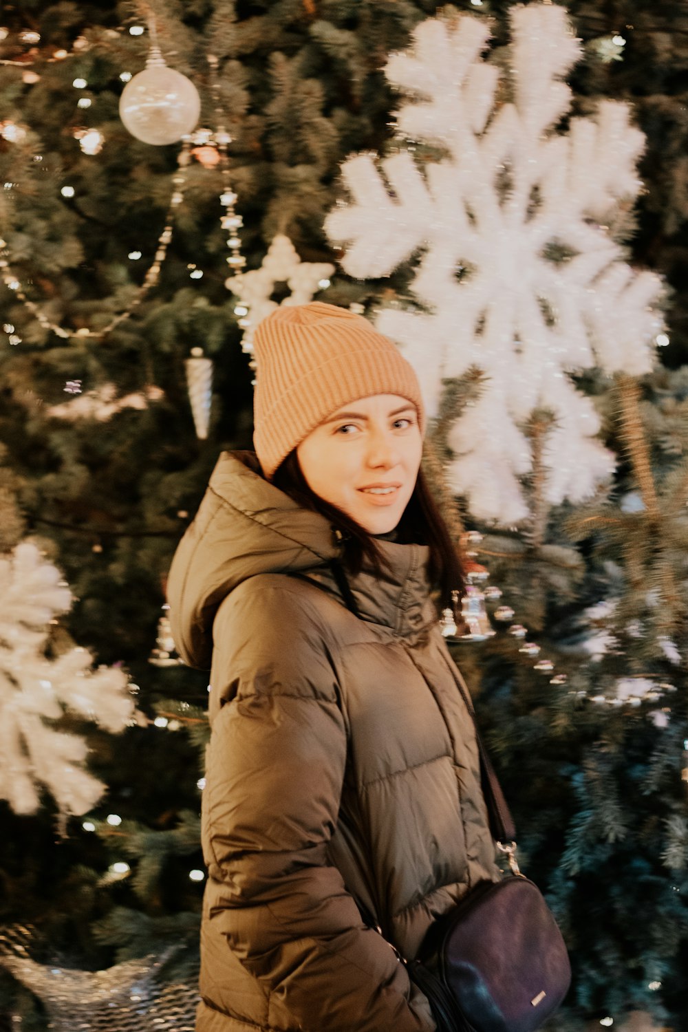 woman in brown knit cap and brown jacket standing near green trees covered with snow during