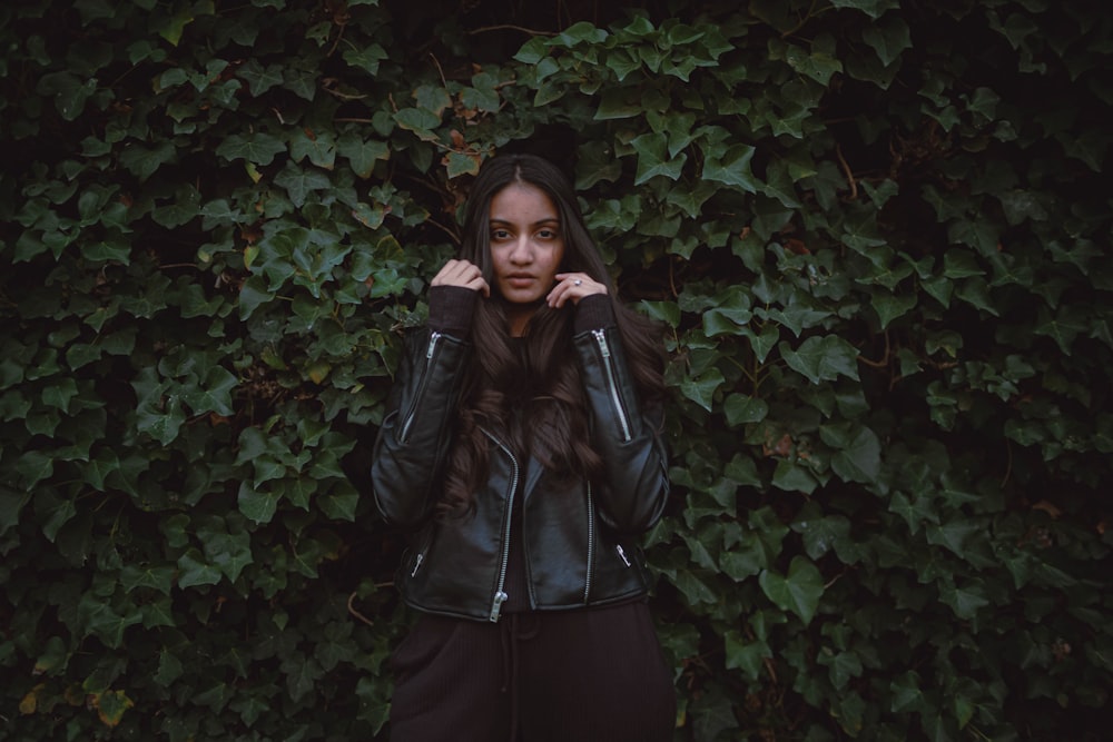 woman in black leather jacket standing beside green plant