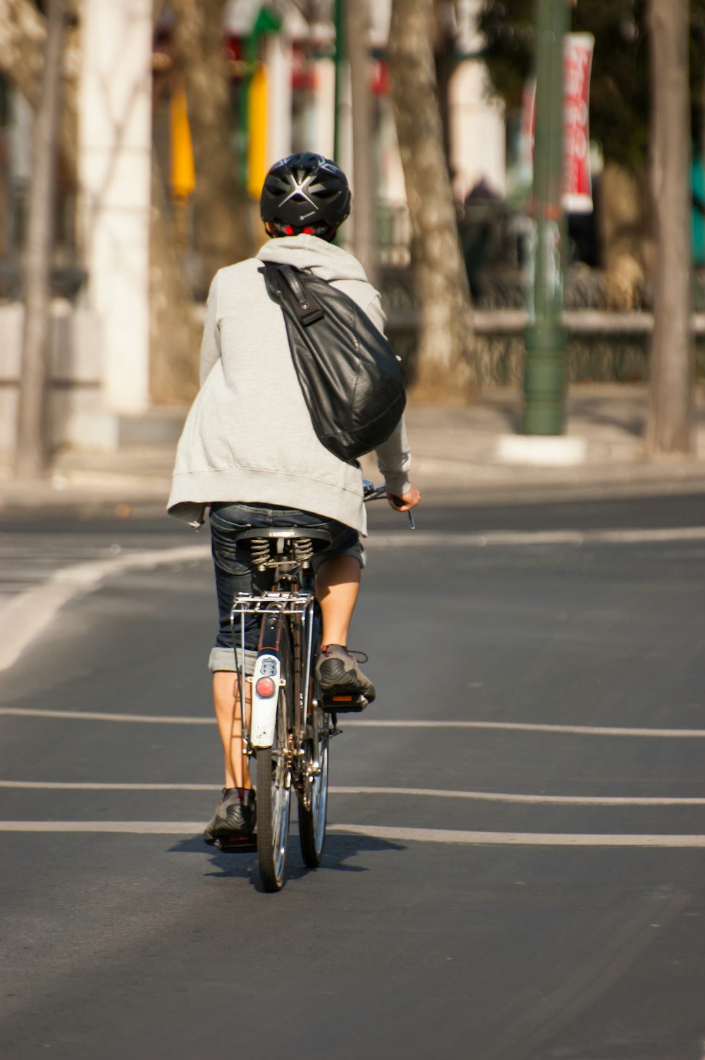 昼間、道路を自転車で走る白いパーカーを着た男性