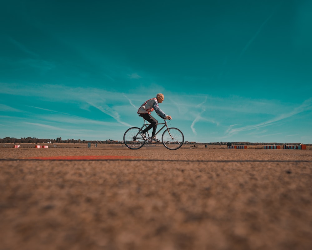 man in black shirt riding bicycle on brown field under blue sky during daytime
