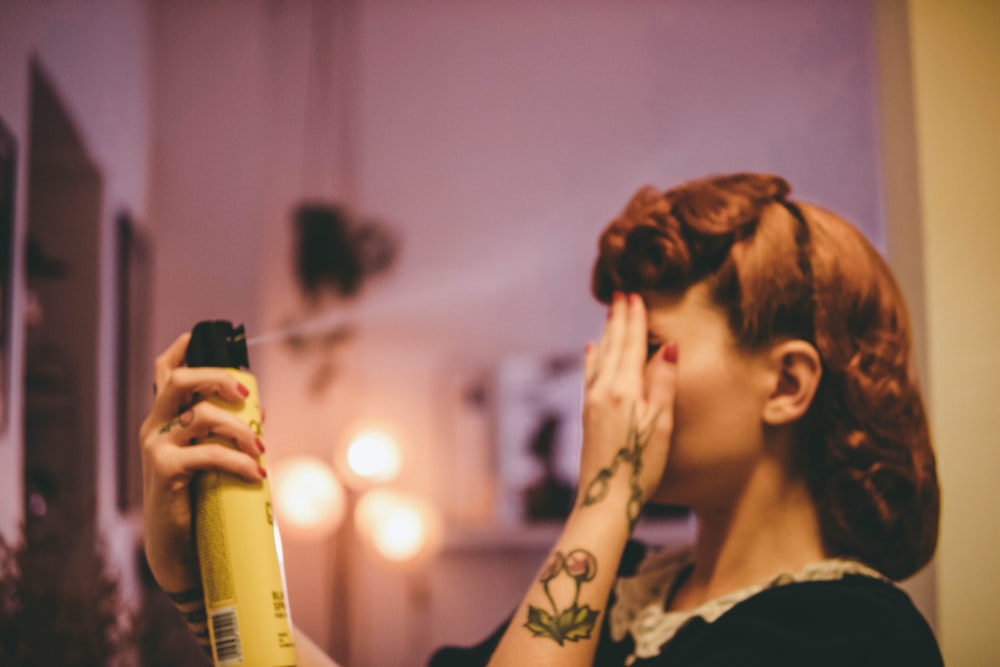 Mujer con camisa floral blanca y negra sosteniendo una botella de spray amarilla y negra