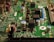 A close-up view of an electronic circuit board featuring various components such as capacitors, resistors, and integrated circuits. The board is mostly green with metallic elements, showing a complex array of electronic architecture.