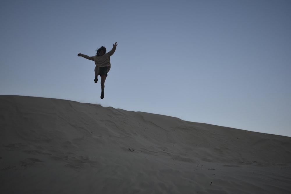 a person jumping in the air on top of a sand dune