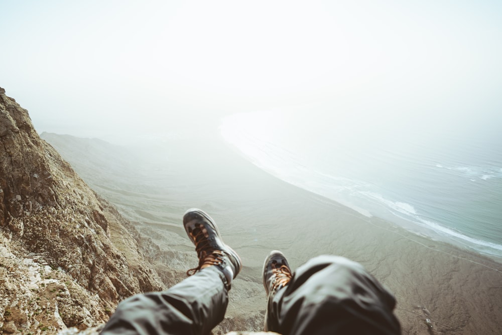 person in black hiking shoes sitting on rock mountain during daytime