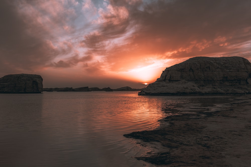 a sunset over a body of water with rocks in the background