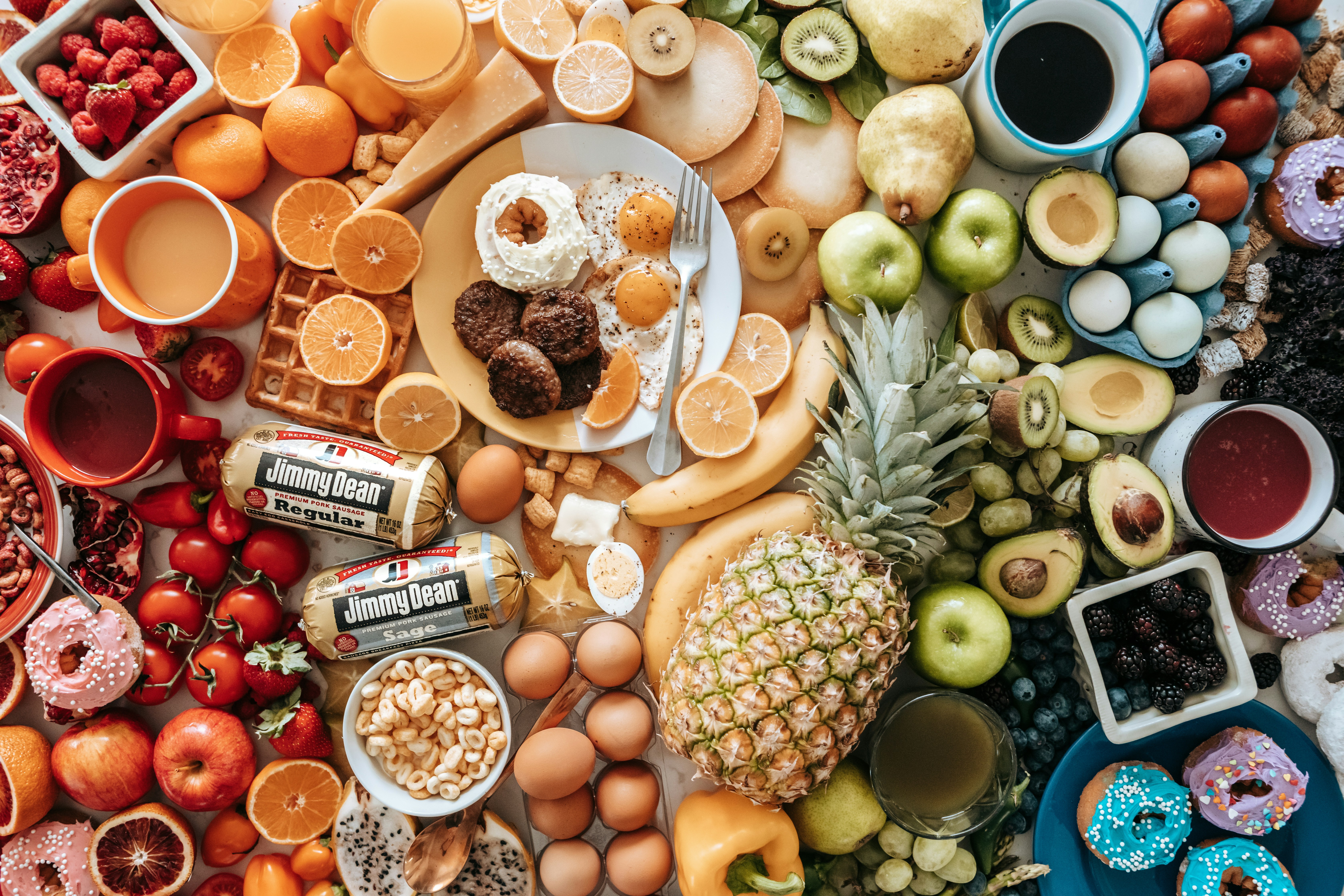 A large assortment of fresh fruit, eggs, breakfast meats, and donuts on a table